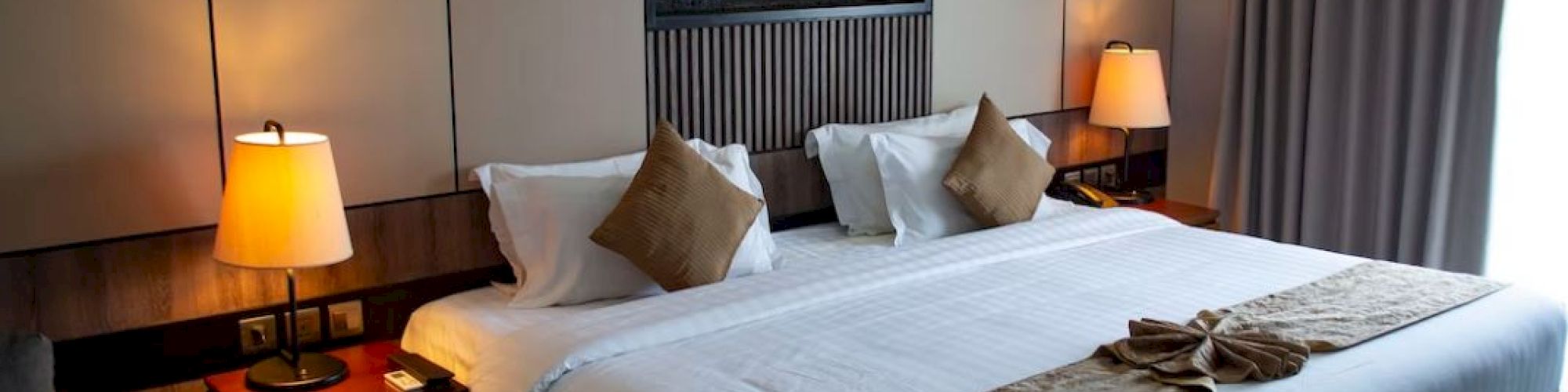 A cozy hotel room featuring a large bed with brown accents, two bedside tables with lamps, and a decorative wall panel, always ending the sentence.