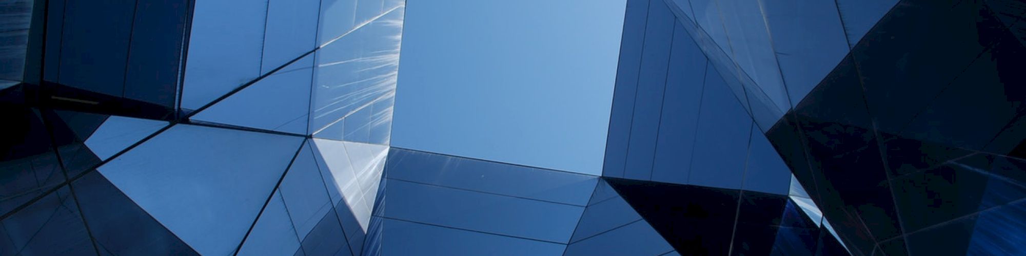 The image shows an abstract architectural design with mirrored surfaces reflecting the sky above, creating a geometric and symmetrical pattern.