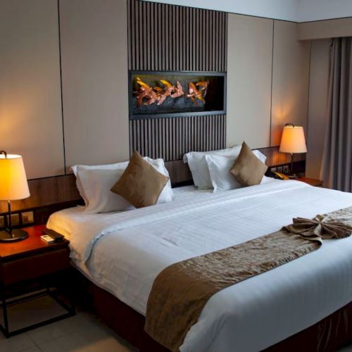 A hotel room with a large bed, two nightstands with lamps, pillows, a wall artwork, and a window with curtains.