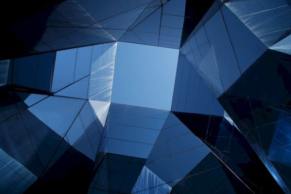 The image shows a geometric view of reflective glass-covered buildings against a blue sky, creating an abstract and symmetrical composition.