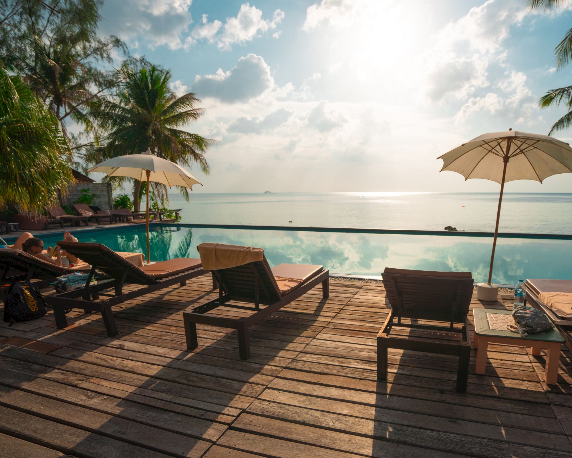 The image shows a serene seaside scene with lounge chairs, umbrellas, and a calm ocean under a partly cloudy sky, creating a tranquil atmosphere.