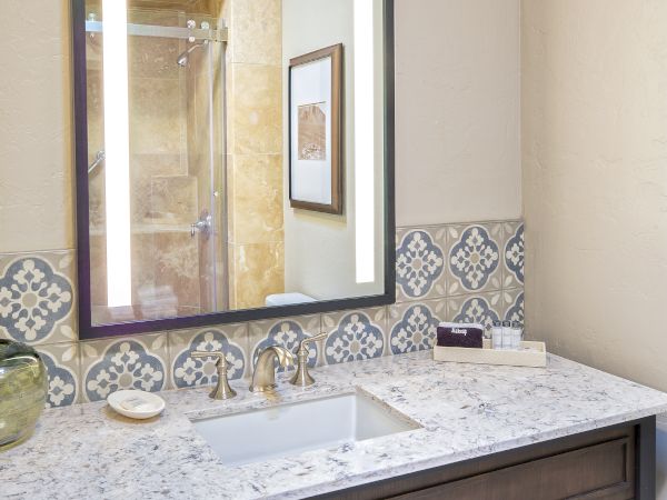 This image shows a bathroom with a decorative mirror, a countertop with a sink, and folded towels on a shelf underneath.