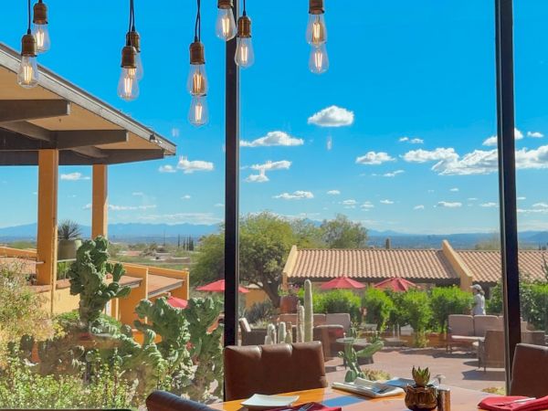 Cozy dining area with wooden tables, hanging light bulbs, and a sunny outdoor view featuring blue skies and desert landscape outside the large windows.
