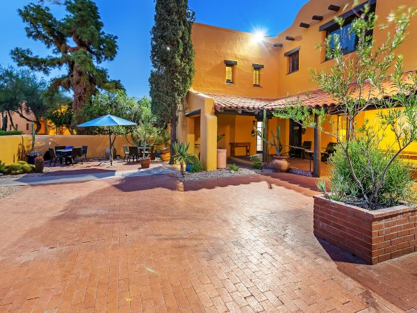 A courtyard featuring a terracotta-colored patio, outdoor seating area with an umbrella, potted plants, and a yellow stucco building with arches.