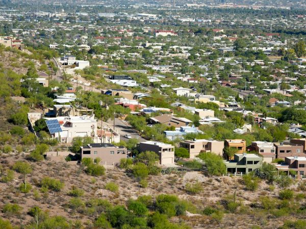 A sprawling suburban neighborhood with houses among hilly and flat terrains, along with scattered green vegetation, is depicted in the image.