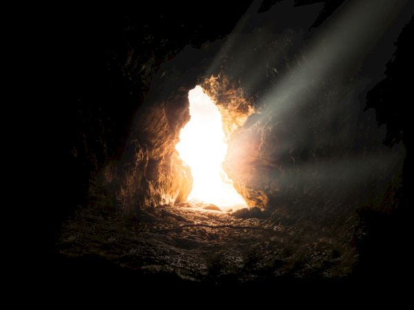 A cave with sunlight streaming through the entrance, illuminating the dark interior.