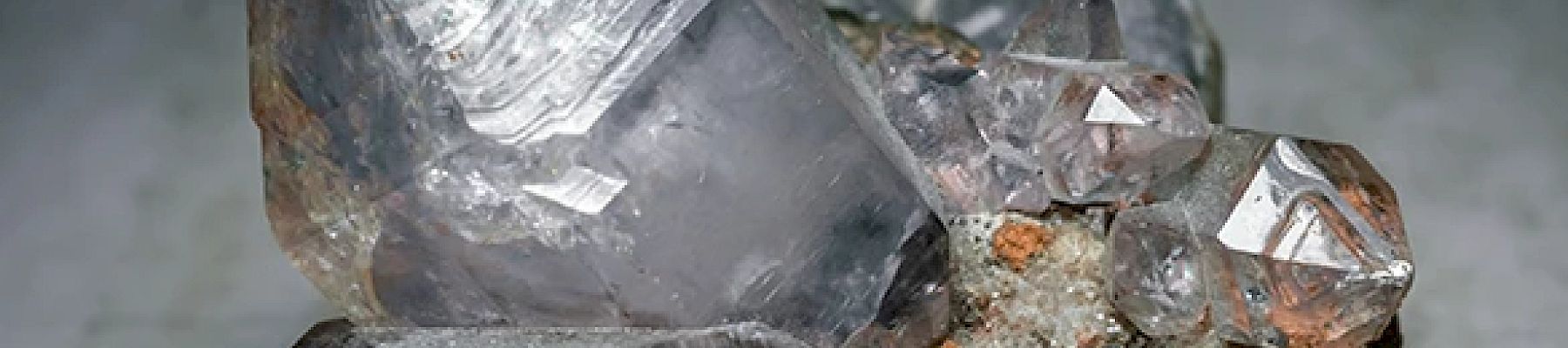 The image shows a cluster of clear, hexagonal quartz crystals attached to a piece of rock, showcasing their natural structure and transparency.
