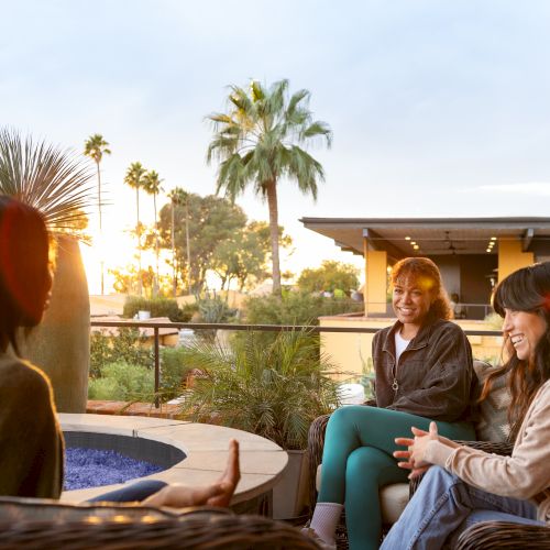 Three people chatting on a patio at sunset, with palm trees in the background.
