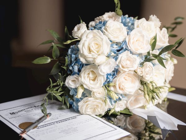 A bouquet of white and blue flowers is placed beside a document with a pen. The bouquet and document are reflected on a black surface.