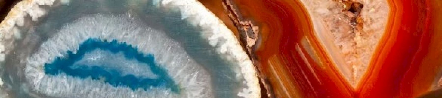 The image shows various mineral geodes, with colorful crystalline structures inside, including a prominent blue and an orange-red geode in the foreground.