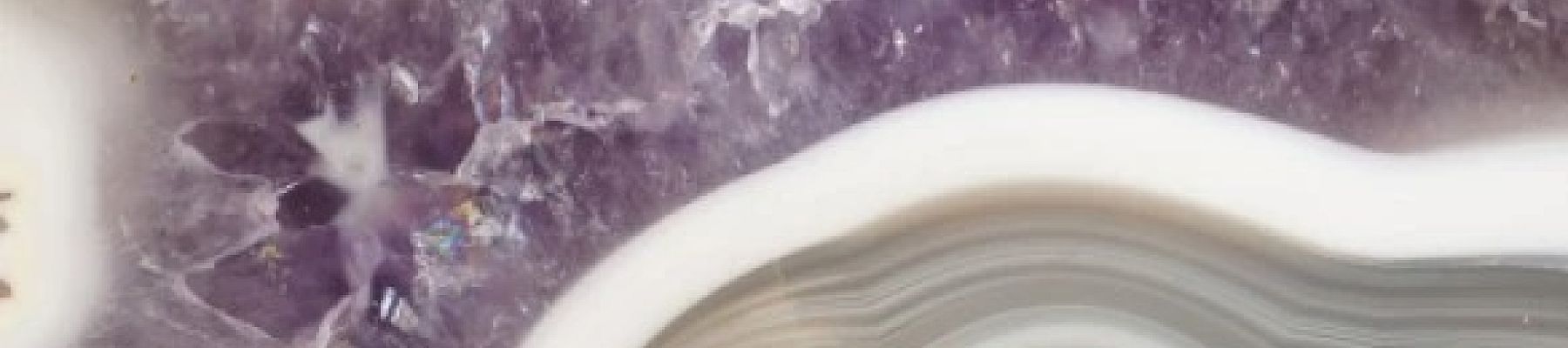 This image shows a close-up of a polished cross-section of a geode with layers of gray, white, and purple minerals.
