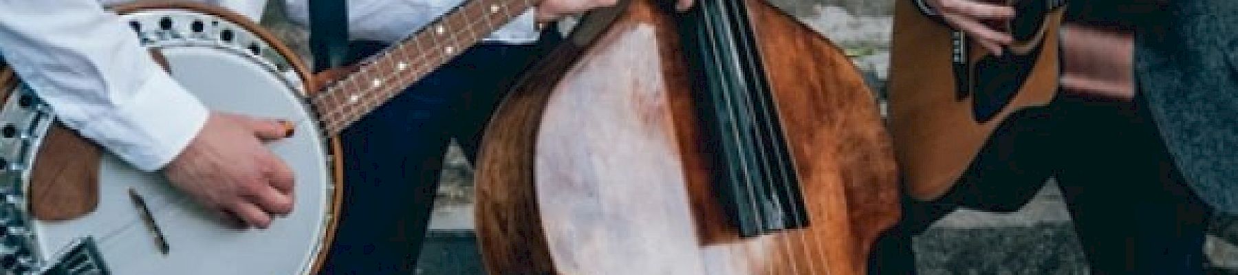 Three musicians play a banjo, double bass, and guitar on stone steps, only their torsos are visible, dressed in casual yet formal attire.