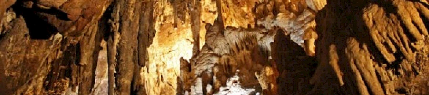 The image shows the interior of a cave with stalactites and stalagmites, illuminated by artificial lighting.