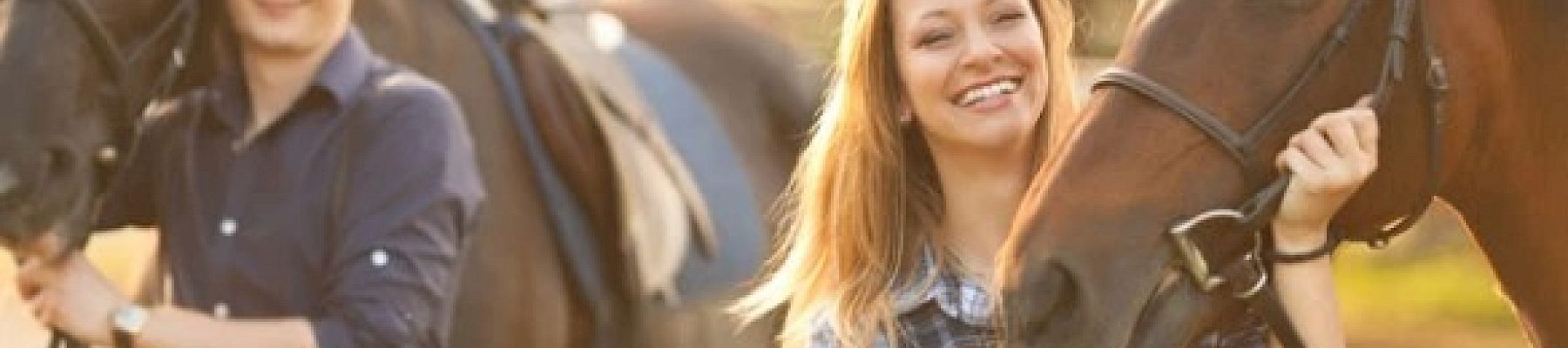 A happy man and woman are holding the reins of two horses in an outdoor setting, both smiling warmly.