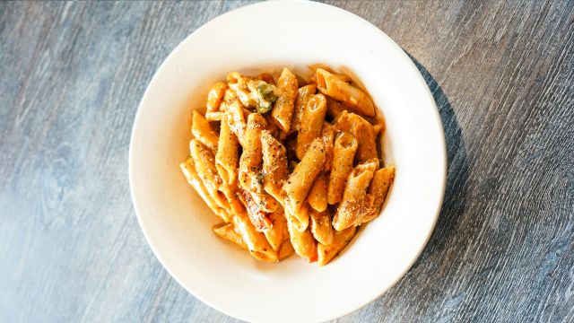 A bowl of penne pasta topped with a reddish sauce and black pepper, placed on a wooden table.