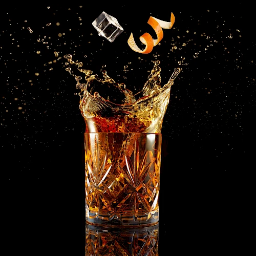 A splash of liquid in a glass with ice and an orange peel against a black background.