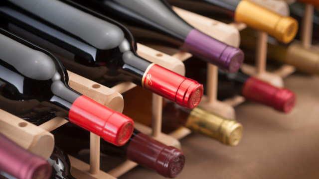 The image shows bottles of wine on a wooden rack, stored horizontally.