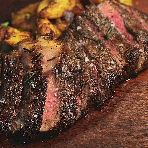 The image shows a sliced, juicy steak on a wooden board, accompanied by crispy roasted potatoes.