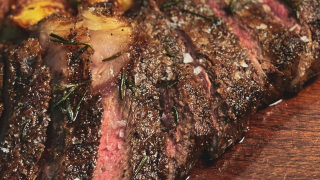 The image shows a sliced, juicy steak on a wooden board, accompanied by crispy roasted potatoes.