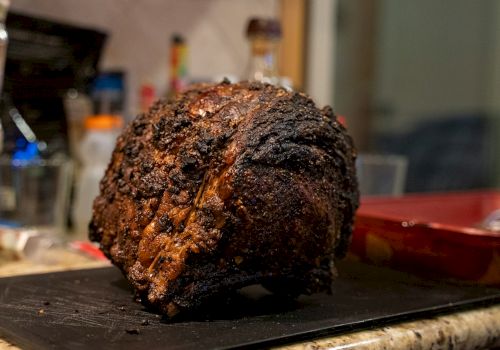 A large, roasted piece of meat on a cutting board in a kitchen setting.