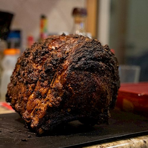 A large, roasted piece of meat on a cutting board in a kitchen setting.