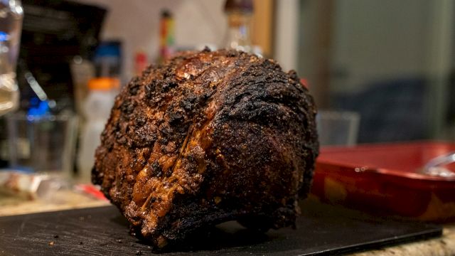 A large, roasted piece of meat on a cutting board in a kitchen setting.