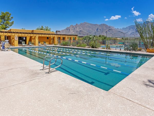 An outdoor swimming pool with lane markers, surrounded by desert landscape and mountains in the background, under a clear blue sky.