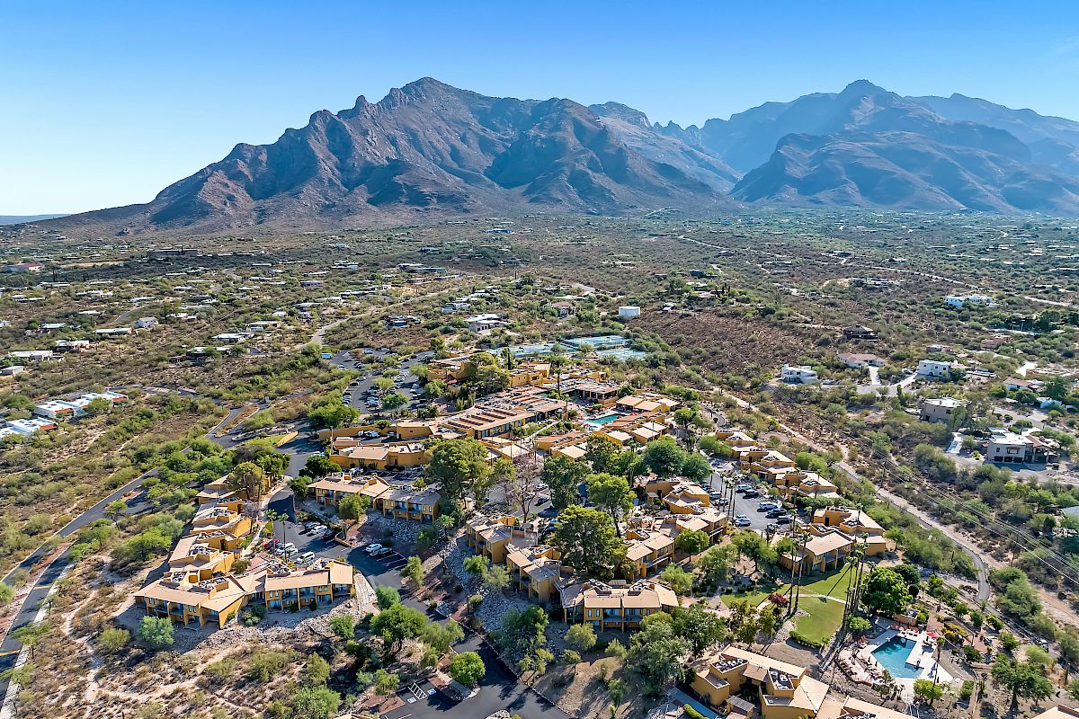 An aerial view of a resort complex surrounded by a desert landscape with mountainous terrain in the background on a clear, sunny day.