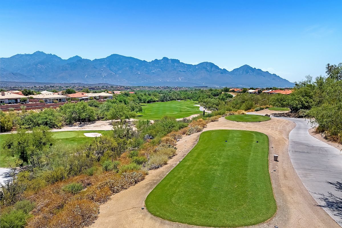 A well-maintained golf course is nestled in a desert landscape with mountains in the background, under a clear blue sky.
