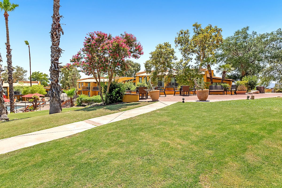 A beautifully landscaped outdoor area with trees, plants, a lawn, and a path leading to a building surrounded by colorful flora.