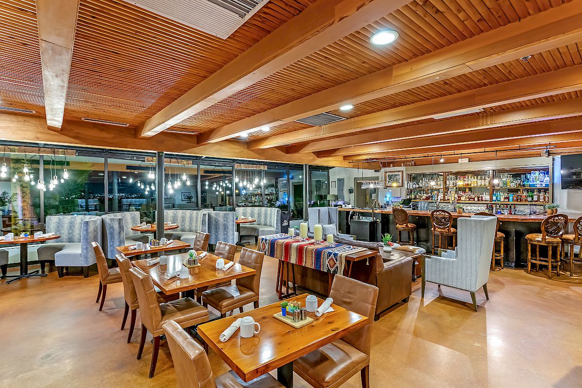 This image shows a warm, inviting restaurant with wooden beams, ample seating, a bar area, and soft lighting creating a cozy atmosphere.