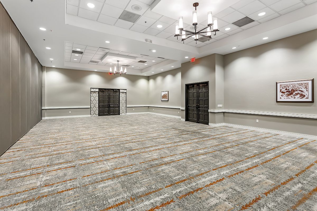 An empty conference room with gray walls, patterned carpet, chandeliers, and double doors, decorated with a picture frame on the wall.