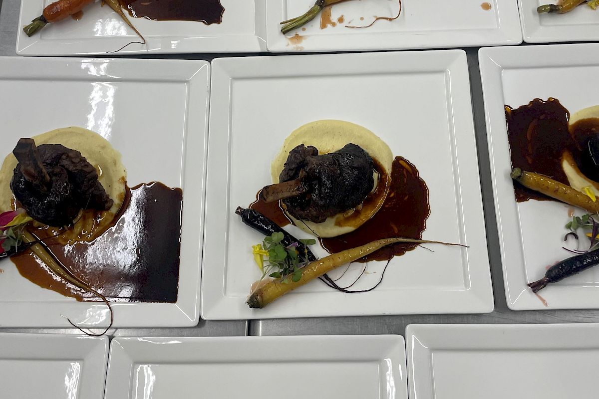 The image shows several plates of gourmet food, each featuring a meat dish, likely braised ribs, with mashed potatoes and garnished vegetables.