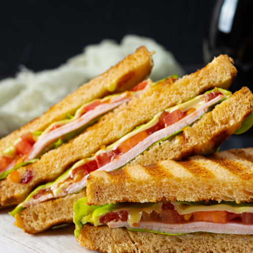 The image shows grilled sandwiches with layers of ham, cheese, lettuce, and tomato, cut into triangles and stacked.