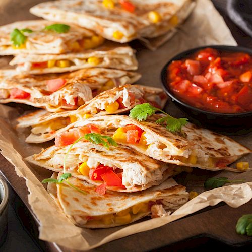 Quesadillas with cheese, corn, and peppers are on a tray, served with a side of salsa and lime wedges.