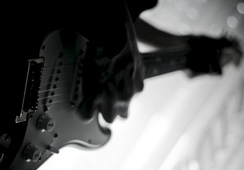 A black and white image of a person playing an electric guitar, captured in a silhouette against a bright background.