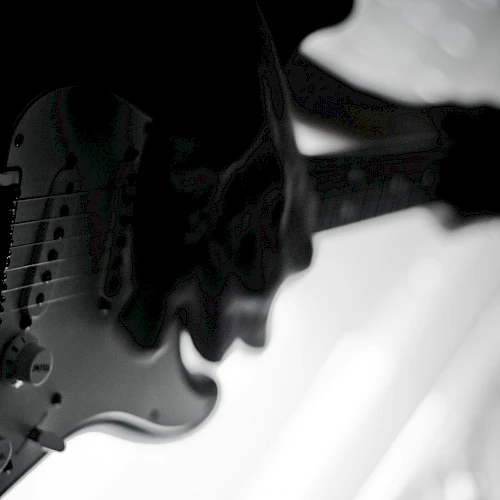 A black and white image of a person playing an electric guitar, captured in a silhouette against a bright background.