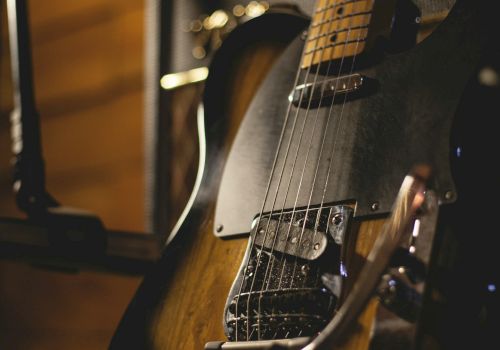 The image shows an electric guitar resting against an amplifier in a dimly lit setting, showcasing its wooden body and strings.