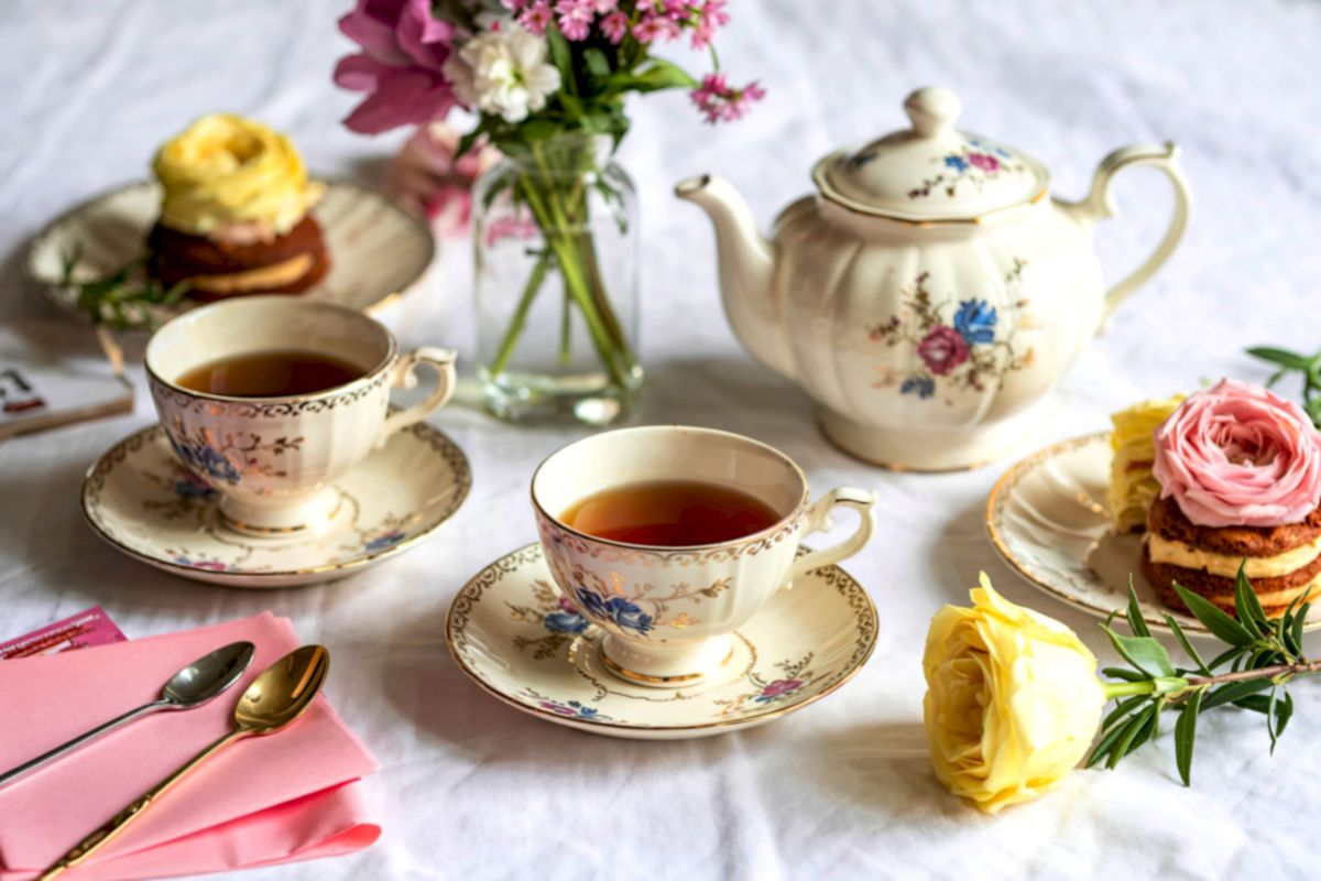 An elegant afternoon tea setup with floral bouquet, teapot, two cups, and pastries on a marble table.