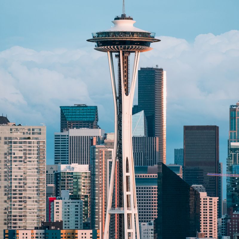 The image features the Space Needle, an iconic observation tower, set against the backdrop of downtown Seattle's modern skyline and buildings.