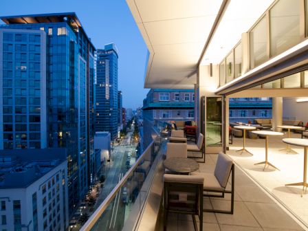 A modern rooftop terrace with city views at dusk, showcasing outdoor seating and tables under ambient lighting, adjacent to an urban high-rise.