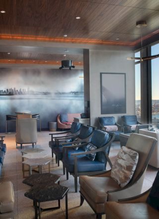 A modern lounge with comfortable seating, large windows offering a scenic water view, and contemporary decor including a cityscape mural on the wall.