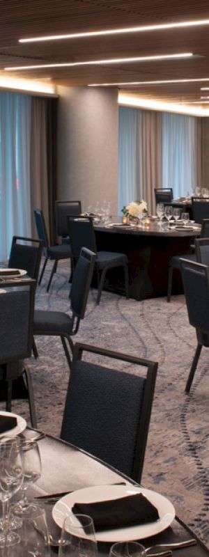 The image shows an elegantly set banquet hall with round tables, place settings, and floral centerpieces under modern lighting fixtures.