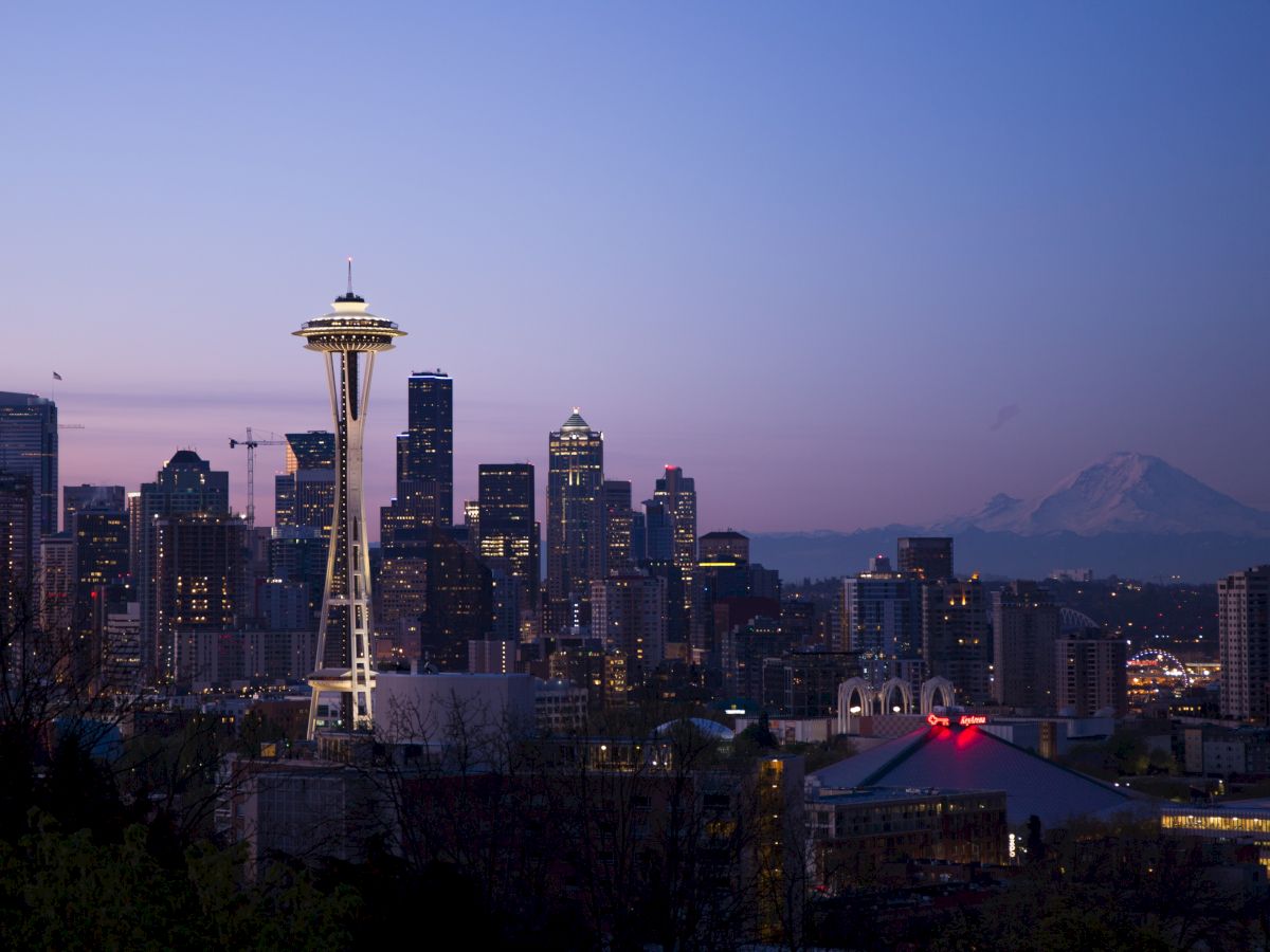 The image shows a cityscape at dusk with prominent skyscrapers, the Space Needle, and a distant mountain.